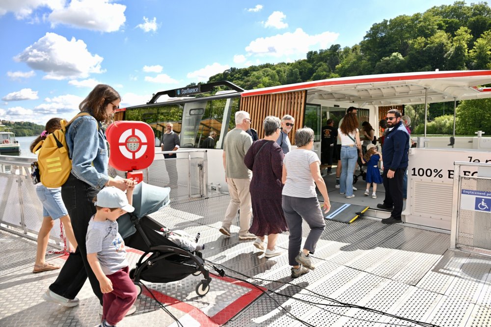 Des passagers montent à bord de la navette fluviale TCL, accueillis par le personnel de navigation, sous un temps ensoleillé